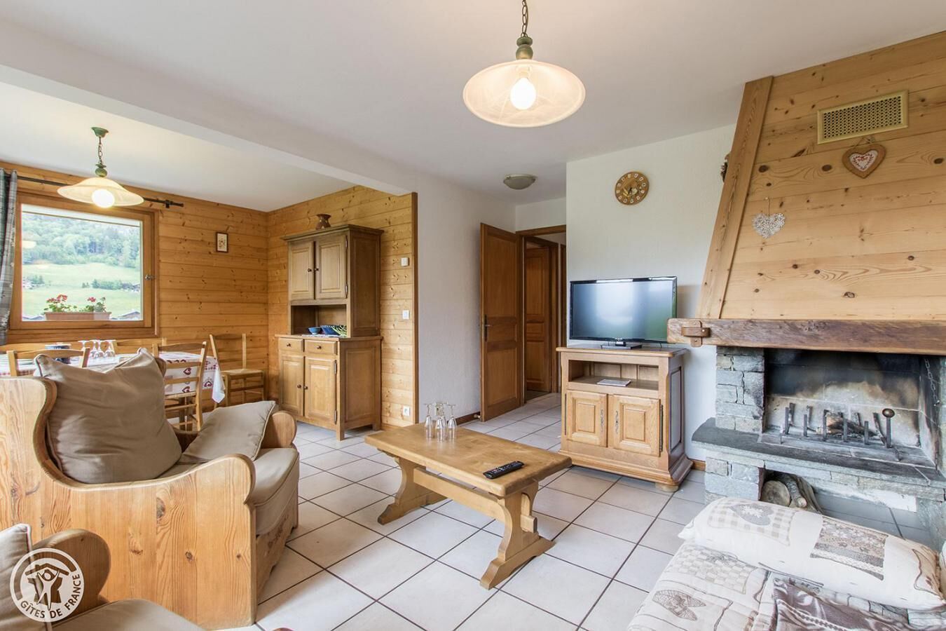 A cozy log cabin interior with a wooden dining area, a sofa, a television, and a fireplace.