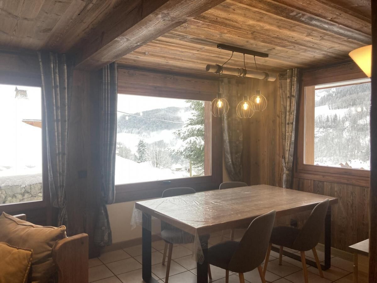 A wooden dining area with a table and chairs, large windows with curtains, and a view of a snowy landscape.