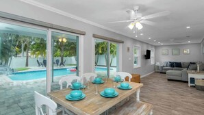 Comedor con una mesa dispuesta para cuatro, ventilador de techo y vista a una piscina a través de puertas de vidrio grandes.