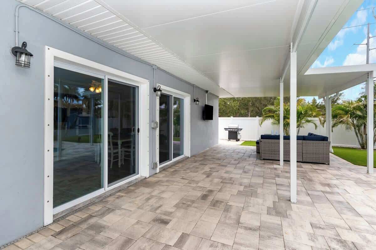 A covered patio area with a tiled floor, sliding glass doors, a seating area with a sofa, and a TV mounted on the wall.