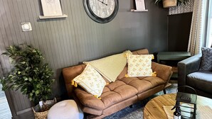 Ein gemütliches Wohnzimmer mit einem braunen Ledersofa, einem runden Holztisch und einem grauen Teppich mit Muster.