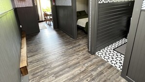 Ein Flur mit Holzboden, einem Bett mit gemustertem Kopfteil und einer Tür zu einem Raum mit Wandverkleidung.