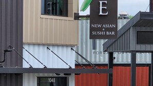 Um edifício com uma placa indicando 'JADE NEW ASIAN SUSHI BAR' e o número '1048' na porta.