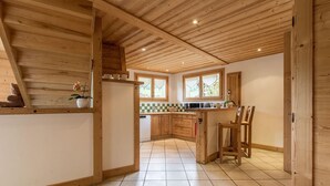 A spacious kitchen with wooden beams, a central island, and a view of the outdoors through large windows.