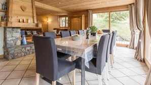 Een ruime eethoek met een lange tafel, meerdere stoelen en een stenen openhaard.