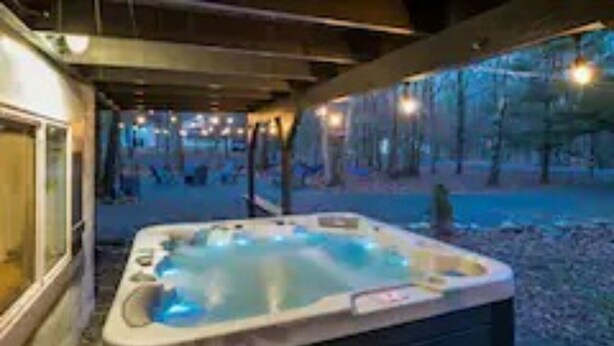 A hot tub in a covered outdoor area with a view of trees and a building in the background. - Zen Escape : Game Room : Hot Tub (Albrightsville)