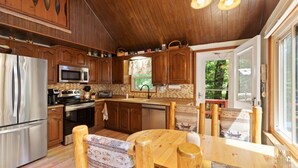 A kitchen with wooden cabinets, stainless steel appliances, and a dining area with a wooden table and chairs. - Zen Escape : Game Room : Hot Tub (Albrightsville)