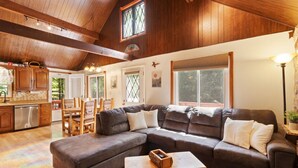 A cozy living room with a sectional sofa, wooden coffee table, and a kitchen area visible through an open door. - Zen Escape : Game Room : Hot Tub (Albrightsville)
