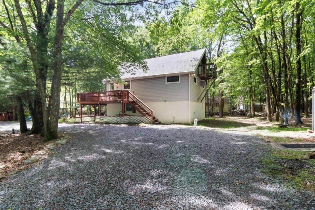 A cabin with a gravel driveway, wooden deck, and a fenced area.