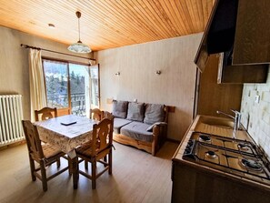 A cozy cabin interior with a dining table, wooden chairs, a sofa, and a kitchen area with a stove. - 1st floor, view mountain, balcony, parking, ski locker, 40m², Le Grand Bornand (Le Grand-Bornand)