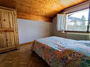 A bedroom with a wooden ceiling, a bed with a colorful bedspread, a window with a view of trees, and a radiator. - 1st floor, view mountain, balcony, parking, ski locker, 40m², Le Grand Bornand (Le Grand-Bornand)