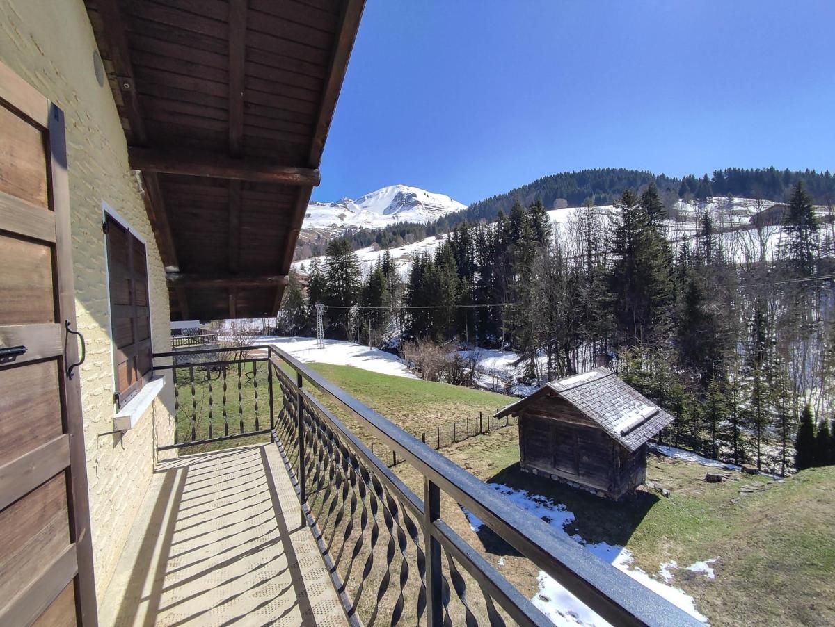 Un balcón de madera con vista a una montaña nevada y una cabaña pequeña.