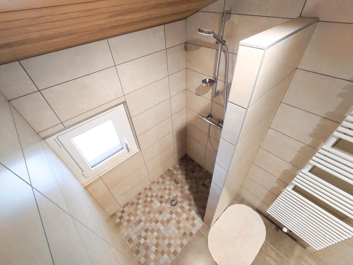 Een kleine badkamer met tegels, een douche, toilet en een raam.