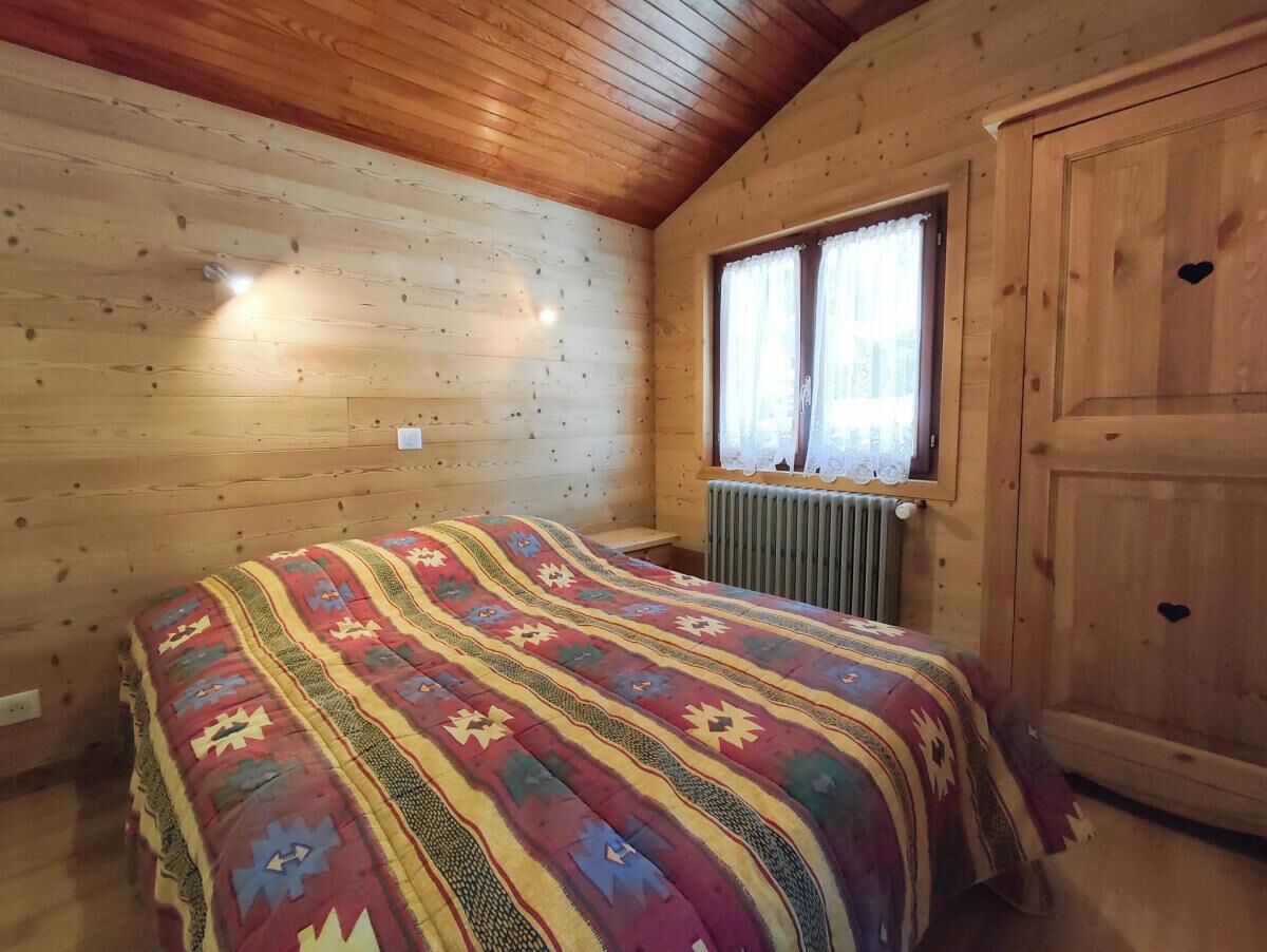 Een gezellig houten kamer met een bed en een kleurrijke sprei, een raam met gordijnen en een radiator.