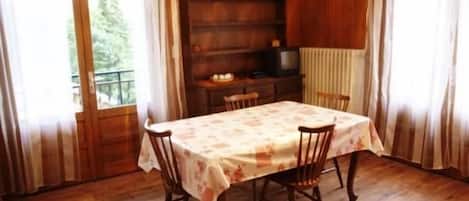 Un comedor con una mesa dispuesta para cuatro personas, sillas de madera, un aparador de madera y un televisor.