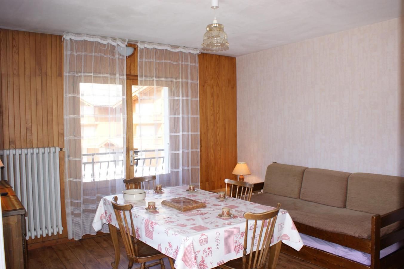 A dining area with a table set for two, a sofa, and a lamp.