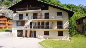 Un immeuble à plusieurs étages, doté de balcons et d’un toit plat, avec une chaîne de montagnes en arrière-plan.