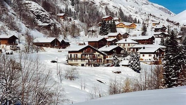 Un village de montagne enneigé, avec des maisons en bois et une piste de ski.