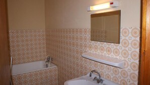 Une salle de bain avec une baignoire, un lavabo, un miroir et une étagère.
