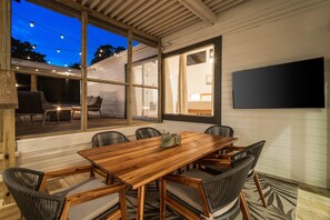 A wooden dining table with six chairs, large windows, and a flat-screen TV mounted on the wall. - Casa Lily*Near Sandestin*PrivateHeatedPool*Bikes* (Miramar Beach)