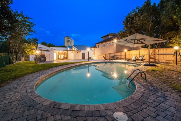 A backyard with a swimming pool, a covered patio area, and a wooden fence.