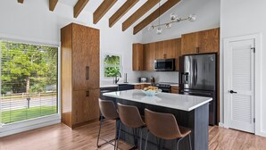 A modern kitchen with wooden cabinets, a central island with bar stools, stainless steel appliances, and a view of the outdoors. - Casa Lily*Near Sandestin*PrivateHeatedPool*Bikes* (Miramar Beach)