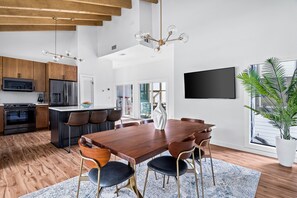 A modern kitchen with wooden cabinets, a central island, and a dining area with a large wooden table and chairs.