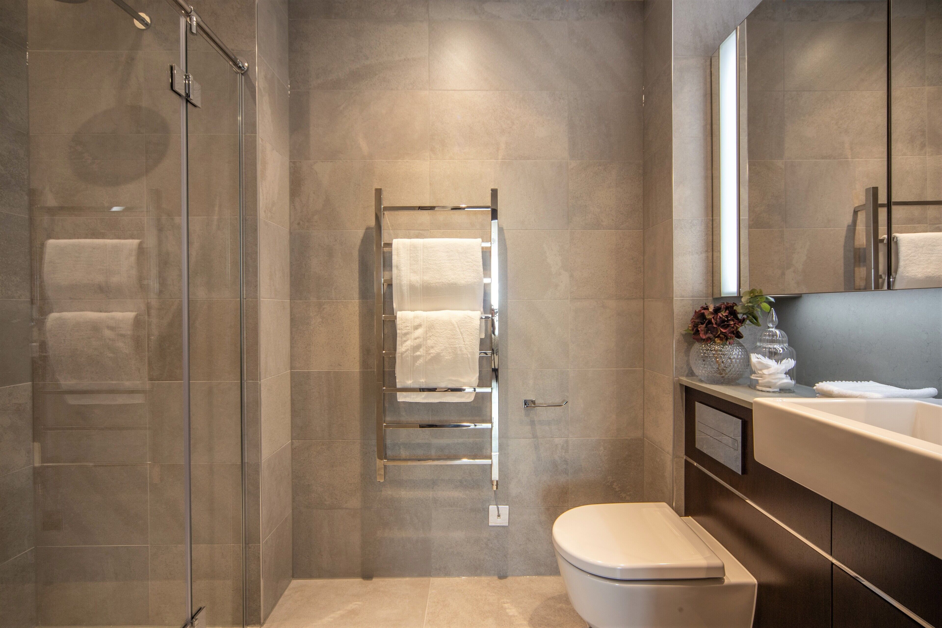 A modern bathroom with a glass shower enclosure, a towel rack, a toilet, and a vanity with a mirror.