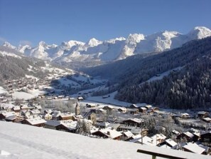 A snow-covered village with traditional houses, a church, and mountains in the background.