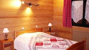 Una habitación de madera con una cama, dos mesitas de noche y una ventana con cortinas.