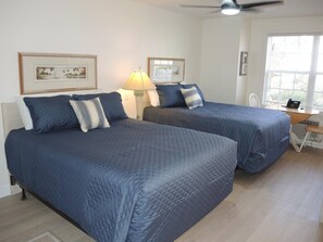 Habitación de hotel con dos camas, un escritorio, una silla y una ventana con persianas.