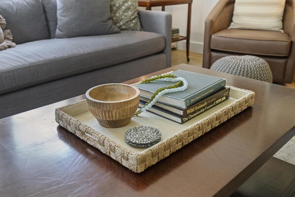 A wooden coffee table with a woven tray holding a bowl, a decorative stone, and books. - Charming Cottage Near Lake Michigan – Walk to Dining, Shops & Bike Trails! (Petoskey)