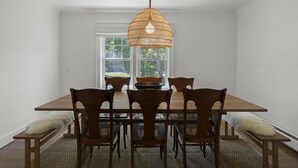 Comedor con mesa y sillas de madera, lámpara colgante de fibras tejidas y vistas al verdor a través de una ventana.