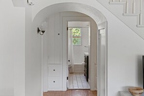 A hallway with a white door leading to a bathroom. - Charming Cottage Near Lake Michigan – Walk to Dining, Shops & Bike Trails! (Petoskey)
