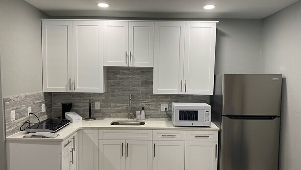 A modern kitchen with white cabinets, a stainless steel refrigerator, a built-in microwave, and a gas stove.