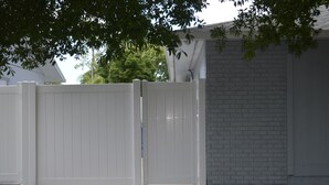 A white wooden fence with a gate, a brick wall, and a tree in the background.