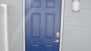 A blue door with a white frame, a doormat with the word "WELCOME," and a light fixture on the wall.