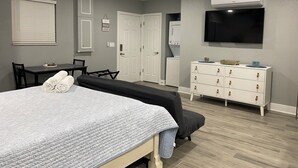 A bedroom with a bed, a desk, a chair, a dresser, and a TV.