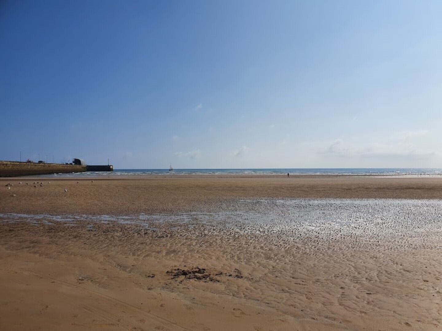 A wide sandy beach with a calm sea and a clear sky.