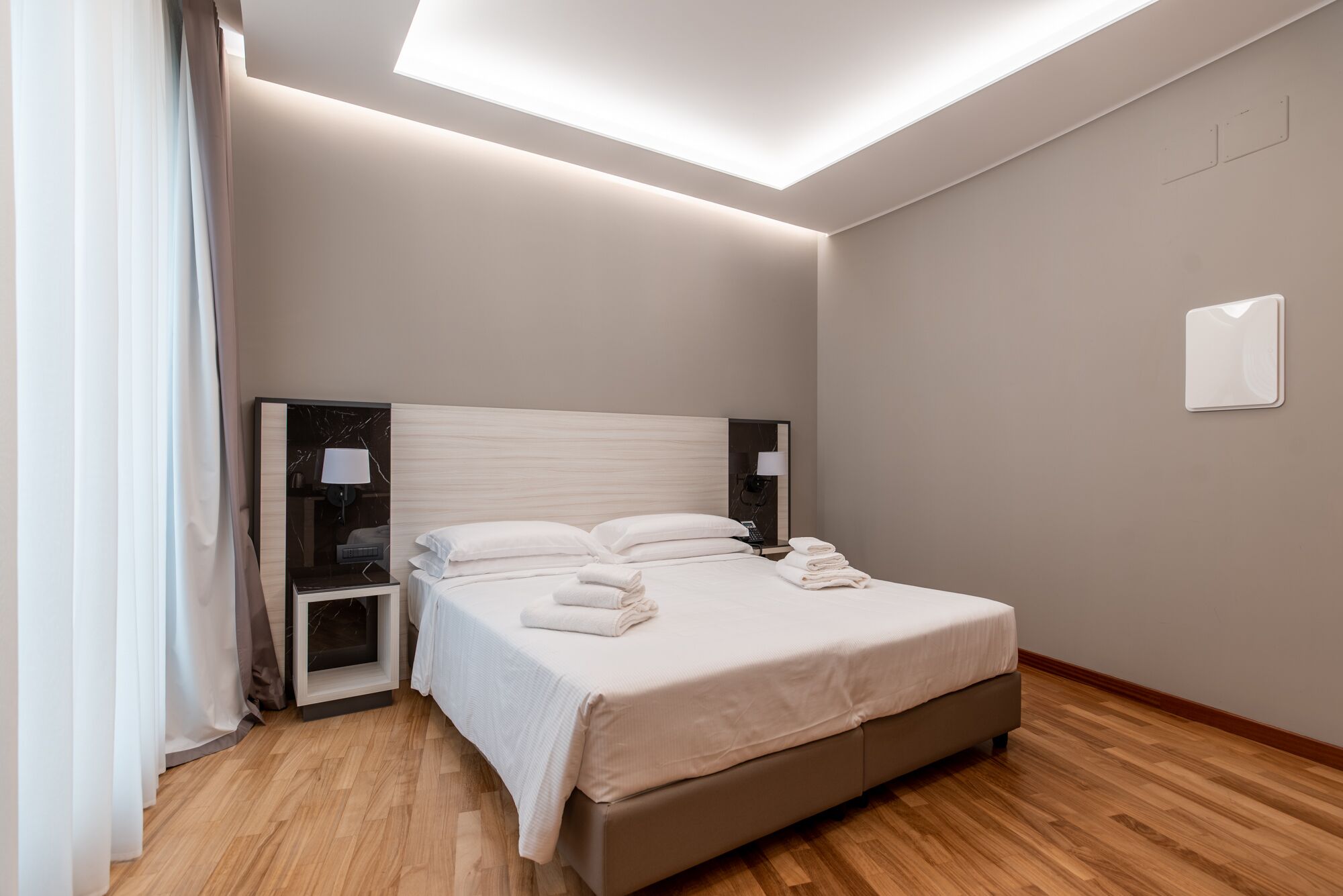 Una habitación de hotel moderna con una cama grande, mesitas de noche, un televisor de pantalla plana y una lámpara en el techo.