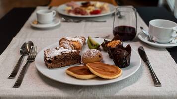 A breakfast setting with plates of pastries, a glass of red wine, and dining utensils on a table.