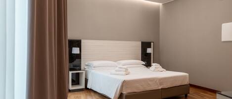 Una habitación de hotel moderna con una cama grande, mesitas de noche y una lámpara en el techo.