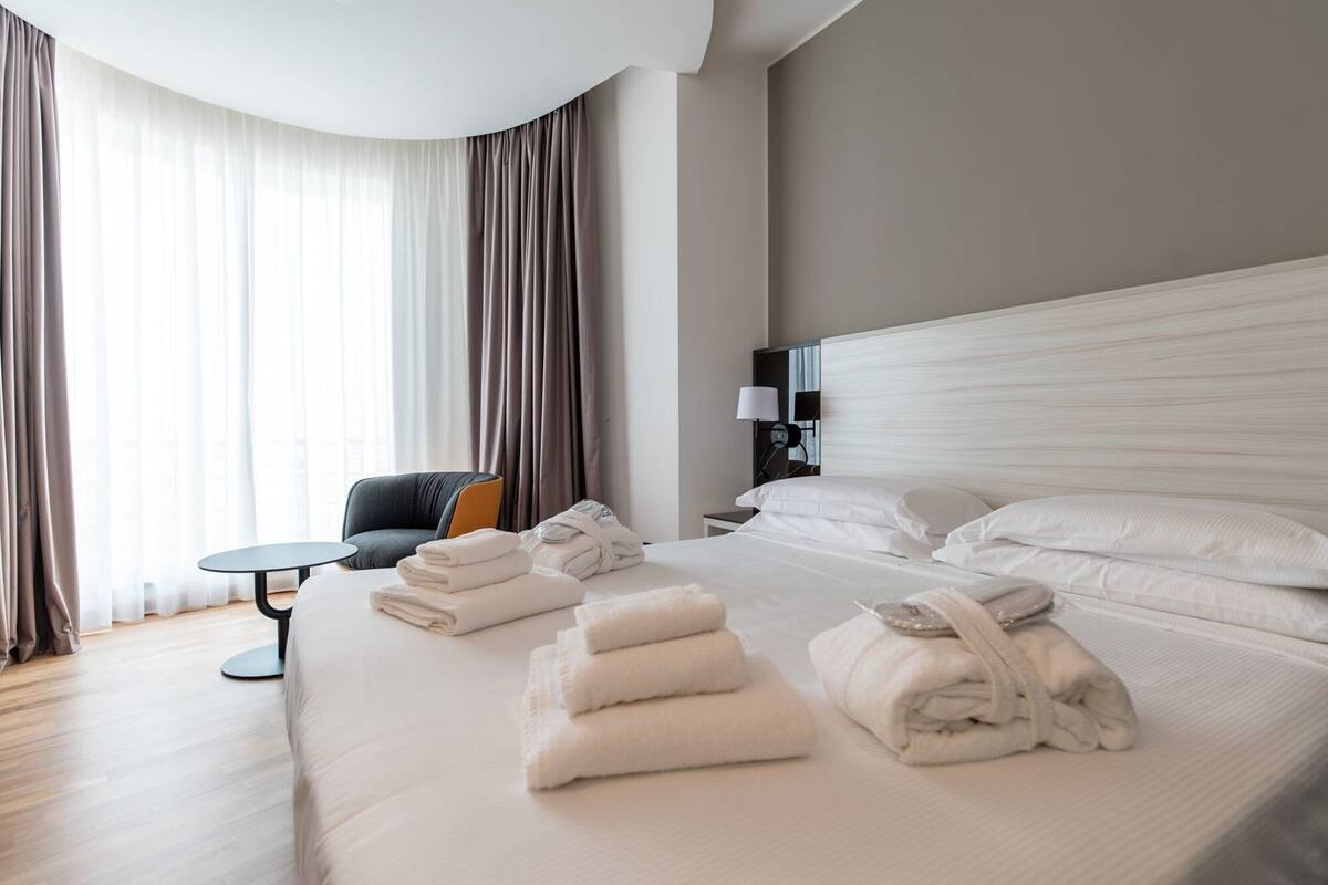 A hotel room with a large bed, a round table, a chair, and a nightstand with a lamp.
