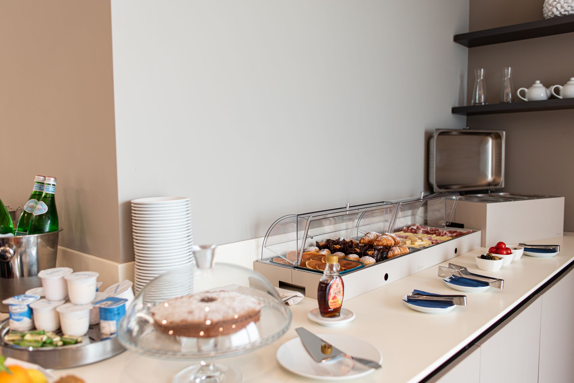 A buffet setup with various food items, including pastries and a cake, and a selection of beverages in the background.