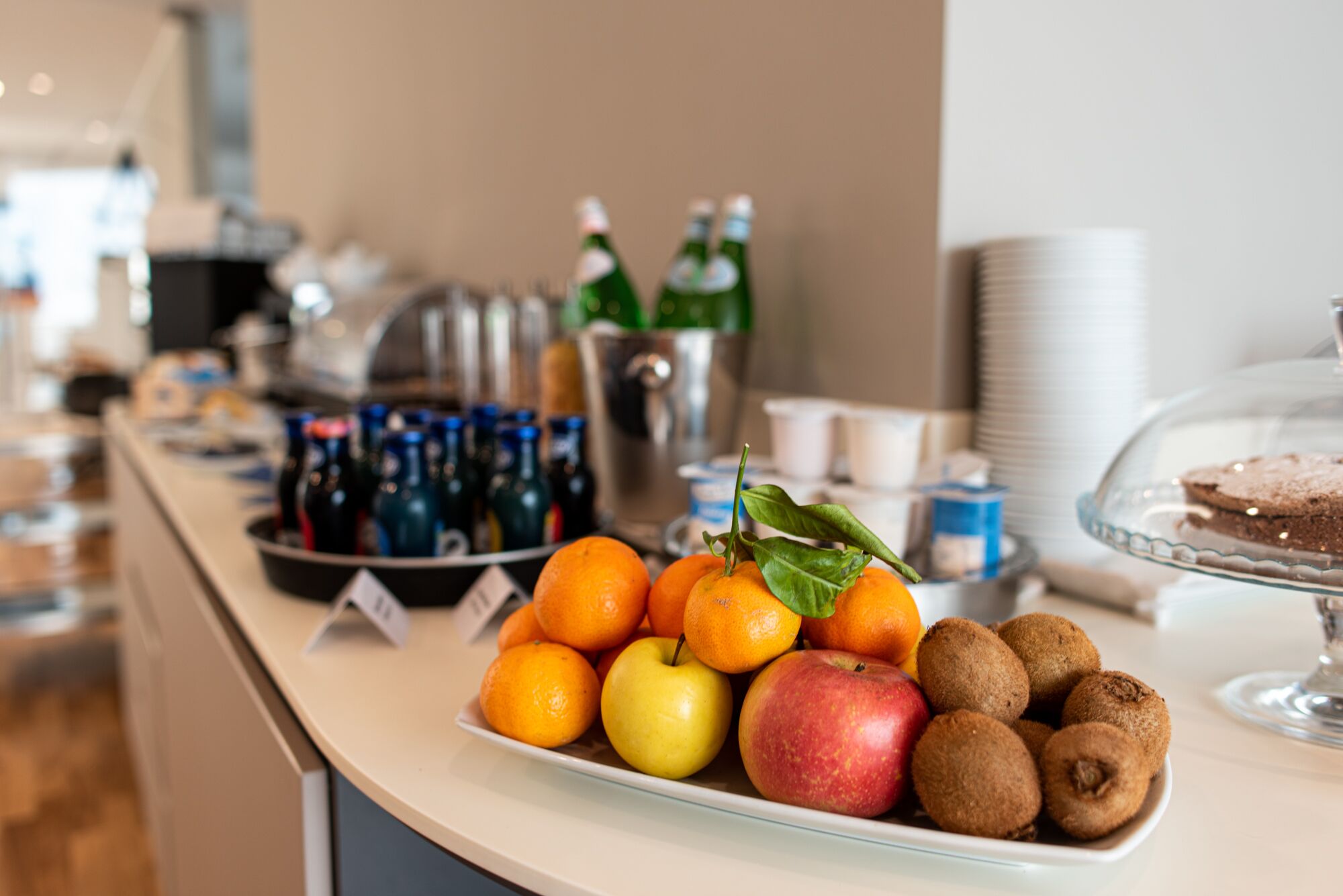A buffet table with fruits, beverages, and a dessert display.