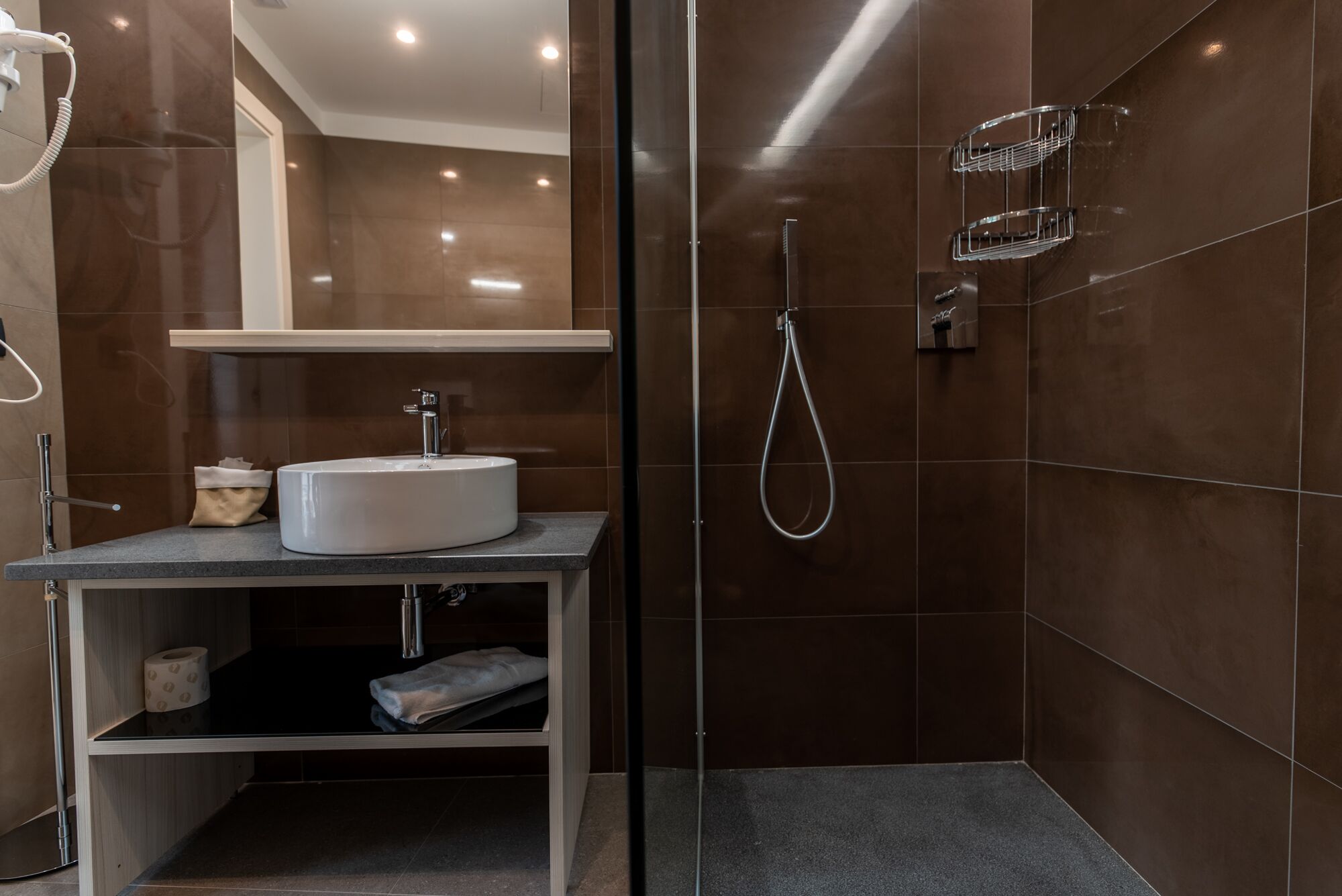 Un baño moderno con cabina de ducha de vidrio, lavamanos blanco y toallero.