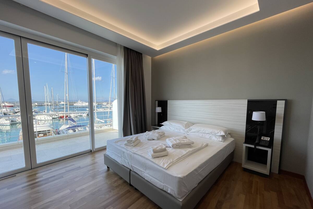 A modern hotel room with a large bed, a nightstand, and a view of a marina.