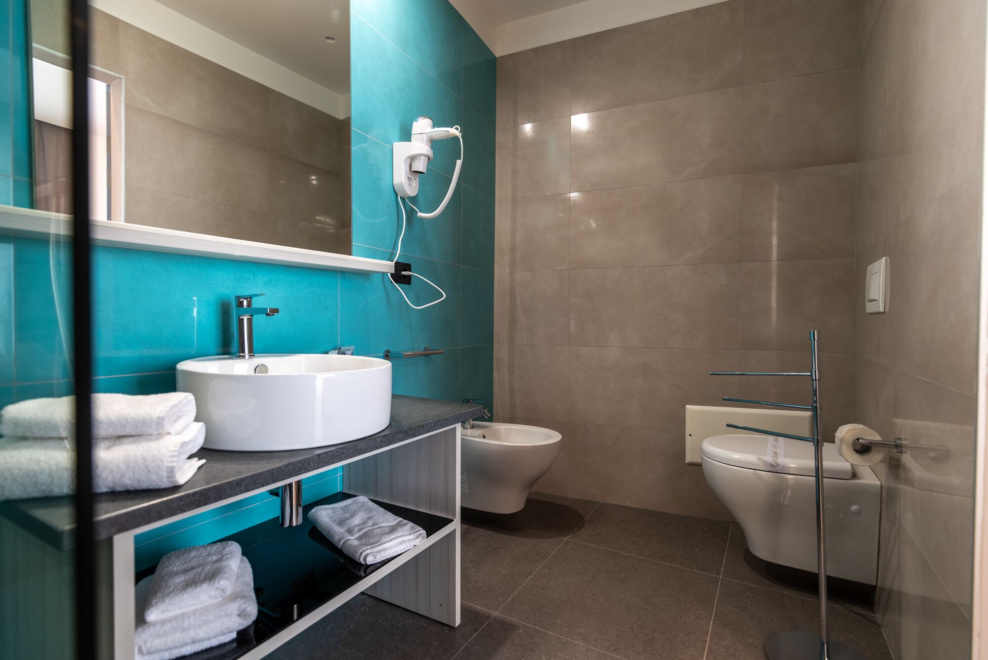 Un baño moderno con un espejo grande, dos lavamanos, inodoro y zona de ducha.