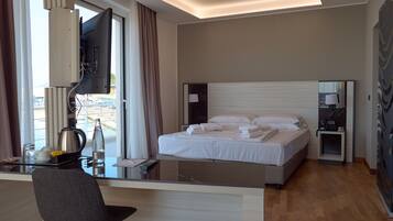 Habitación de hotel con cama, mesita de noche, escritorio, silla y un gran ventanal con cortinas.