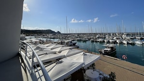 A marina with numerous sailboats docked, a clear sky, and outdoor seating with umbrellas.